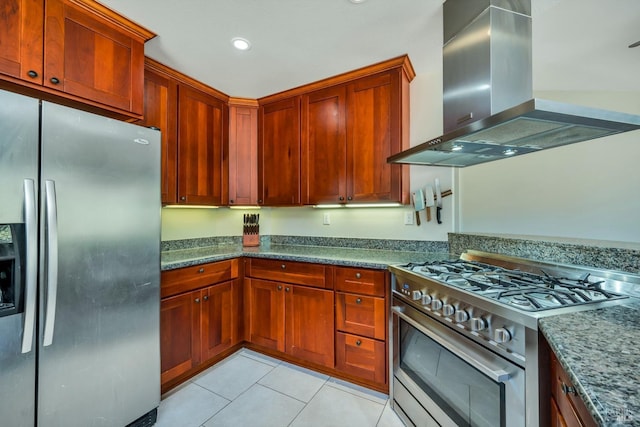 kitchen featuring light tile patterned floors, wall chimney range hood, dark stone countertops, and appliances with stainless steel finishes