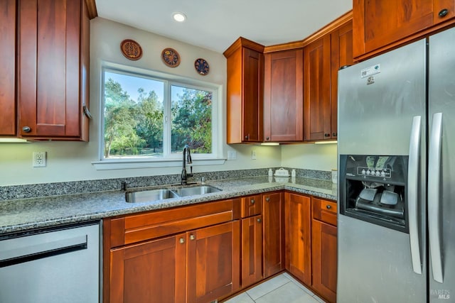 kitchen with dark stone counters, sink, light tile patterned flooring, and stainless steel appliances