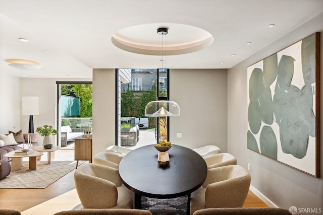 dining space with a raised ceiling and light wood-type flooring