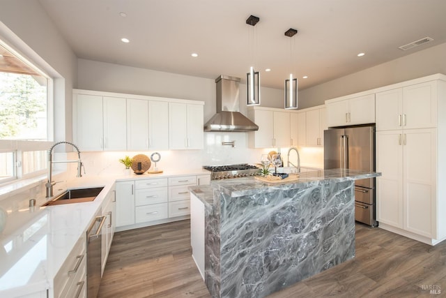 kitchen featuring wall chimney range hood, appliances with stainless steel finishes, a kitchen island, dark hardwood / wood-style flooring, and light stone counters