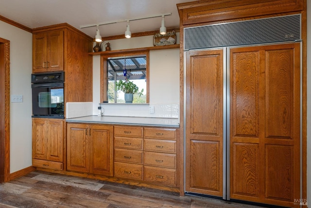 kitchen with paneled built in fridge, hanging light fixtures, crown molding, black oven, and dark hardwood / wood-style flooring