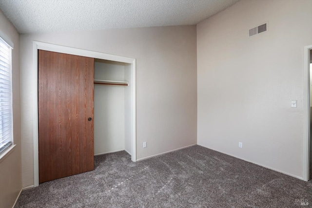 unfurnished bedroom featuring a closet, a textured ceiling, lofted ceiling, and dark colored carpet