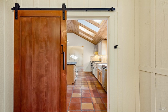 kitchen featuring vaulted ceiling with skylight, a barn door, dark tile patterned floors, tasteful backsplash, and stainless steel appliances