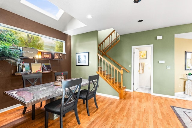 dining area featuring stairway, wood finished floors, baseboards, vaulted ceiling with skylight, and recessed lighting