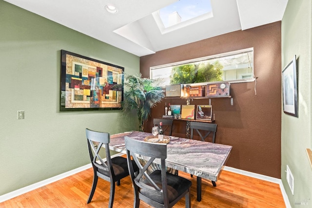 dining space featuring vaulted ceiling with skylight and wood-type flooring