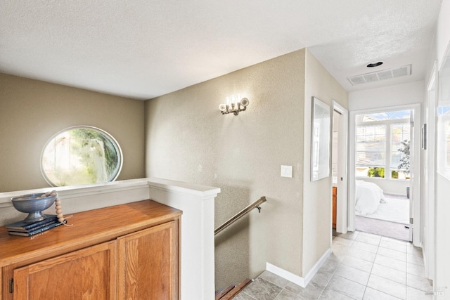 interior space with visible vents, baseboards, an upstairs landing, light tile patterned floors, and a textured ceiling