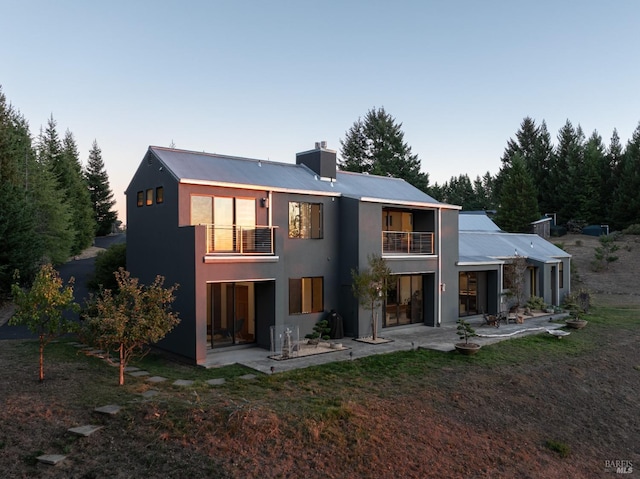 back house at dusk with a balcony and a patio area