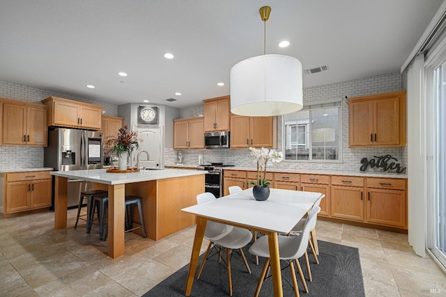 kitchen featuring stainless steel appliances, sink, tasteful backsplash, an island with sink, and pendant lighting