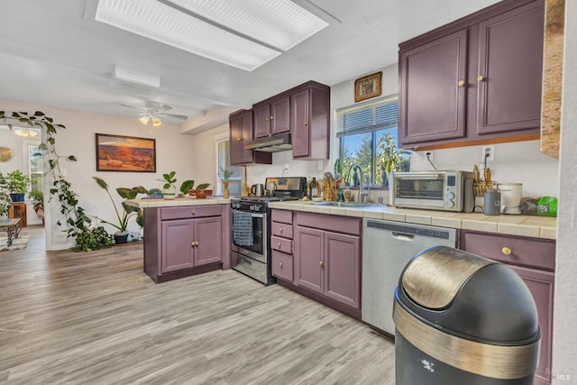 kitchen featuring ceiling fan, sink, stainless steel appliances, light hardwood / wood-style flooring, and tile countertops