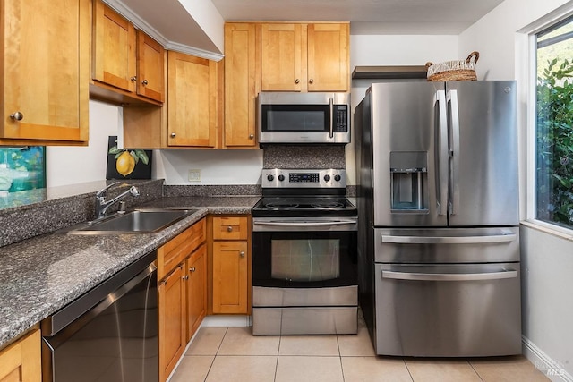 kitchen with baseboards, brown cabinets, appliances with stainless steel finishes, a sink, and light tile patterned floors