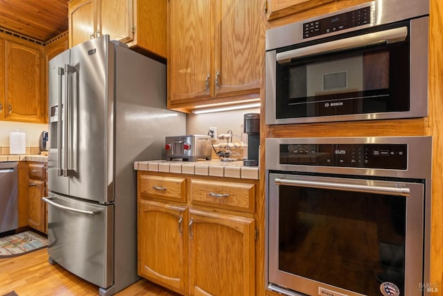 kitchen featuring appliances with stainless steel finishes, light wood-type flooring, and tile counters