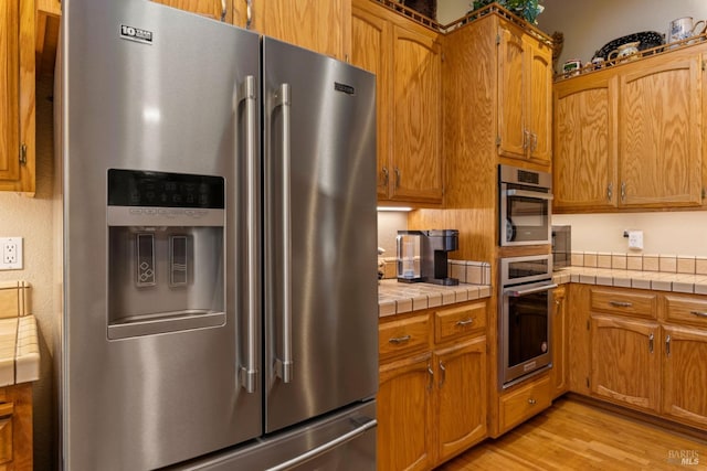 kitchen featuring tile countertops, stainless steel appliances, and light hardwood / wood-style floors