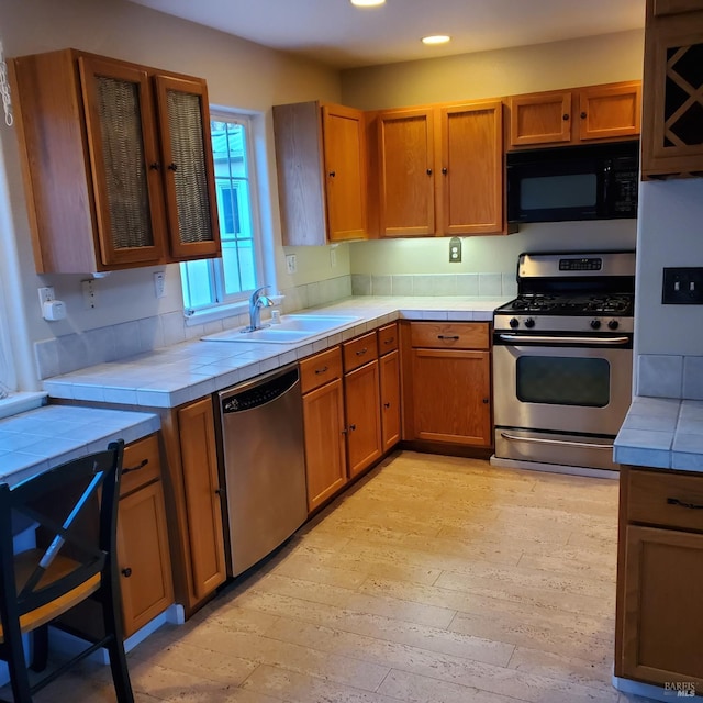 kitchen featuring tile countertops, sink, stainless steel appliances, and light hardwood / wood-style flooring