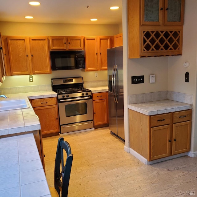 kitchen with appliances with stainless steel finishes, tile countertops, light hardwood / wood-style flooring, and sink