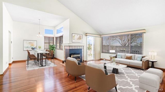 living area featuring a chandelier, wood finished floors, high vaulted ceiling, a tile fireplace, and baseboards