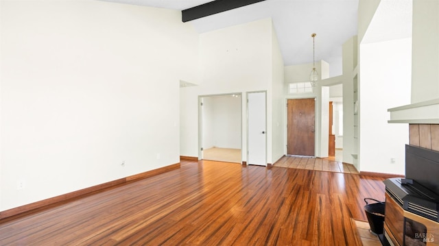 unfurnished living room with high vaulted ceiling, wood finished floors, beam ceiling, and baseboards