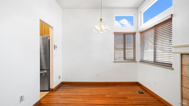 unfurnished dining area with a textured ceiling, a notable chandelier, wood finished floors, visible vents, and baseboards