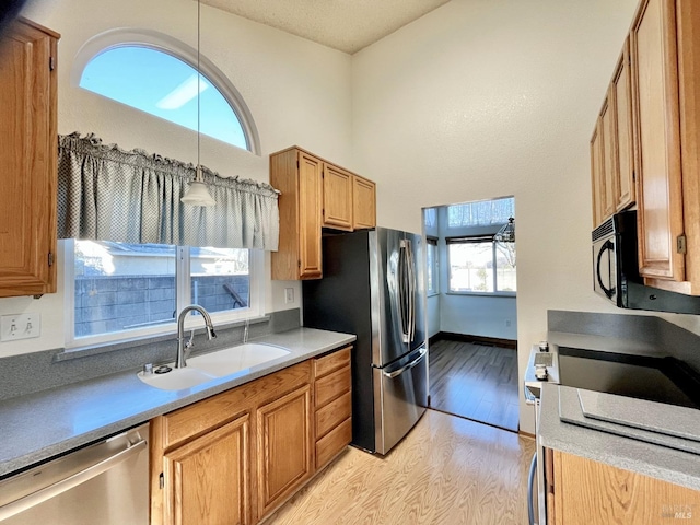 kitchen featuring sink, hanging light fixtures, light hardwood / wood-style flooring, stainless steel appliances, and a high ceiling