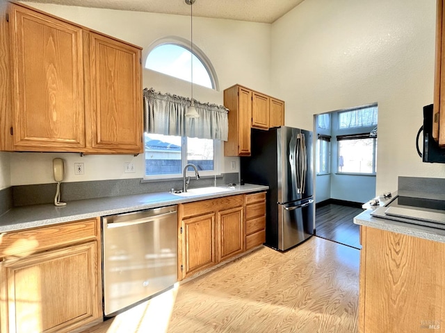 kitchen featuring appliances with stainless steel finishes, decorative light fixtures, sink, and light hardwood / wood-style flooring