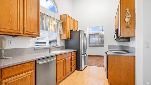 kitchen featuring a sink, baseboards, appliances with stainless steel finishes, light wood finished floors, and brown cabinetry