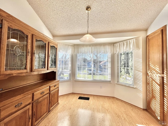 dining space featuring vaulted ceiling, a textured ceiling, and light hardwood / wood-style floors