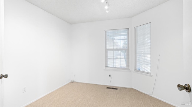 carpeted spare room featuring a textured ceiling, rail lighting, visible vents, and baseboards