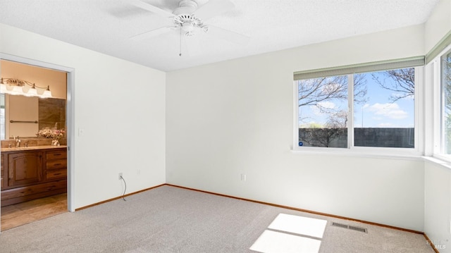 unfurnished bedroom with a textured ceiling, a sink, visible vents, and light colored carpet