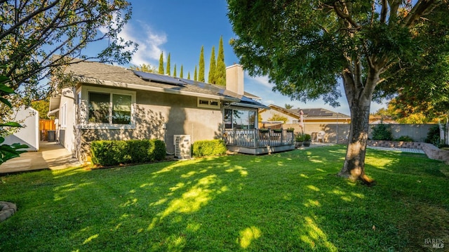 rear view of house with a wooden deck, a yard, and solar panels