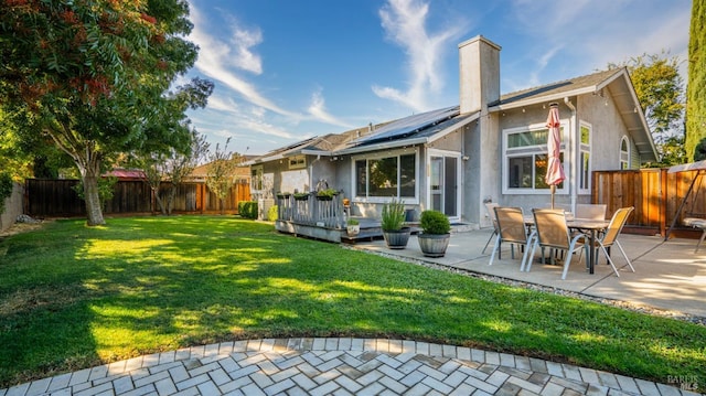 back of house with a wooden deck, a yard, a patio area, and solar panels