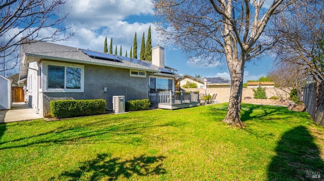 back of property featuring solar panels, stucco siding, a lawn, a fenced backyard, and a wooden deck