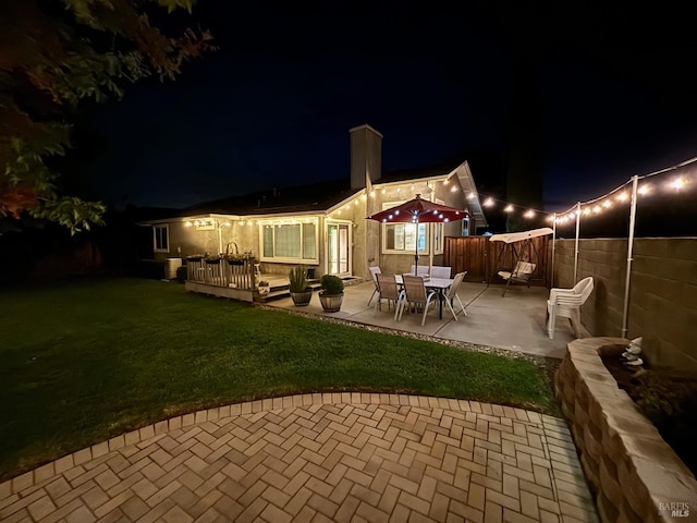 back house at twilight featuring a patio area and a lawn