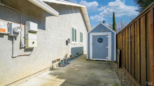 view of side of home with an outbuilding, a patio, fence, stucco siding, and a storage unit