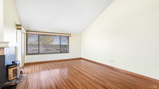 unfurnished living room with lofted ceiling, a wood stove, baseboards, and wood finished floors