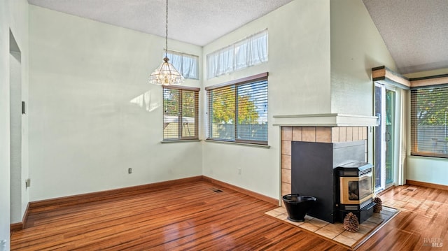 unfurnished living room with a healthy amount of sunlight, a textured ceiling, wood-type flooring, and a wood stove