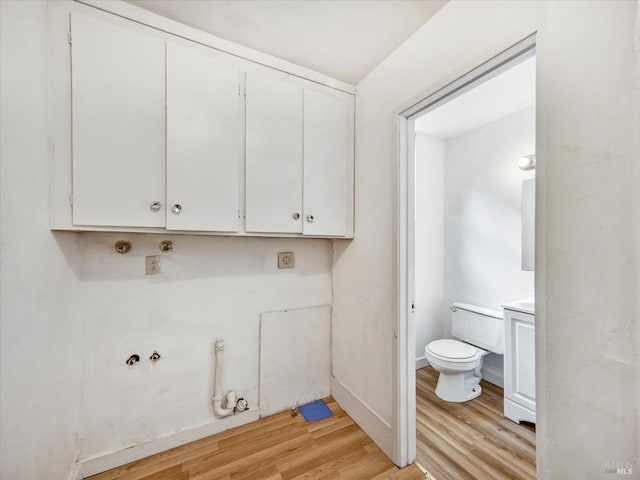 laundry room with gas dryer hookup, light hardwood / wood-style flooring, and cabinets