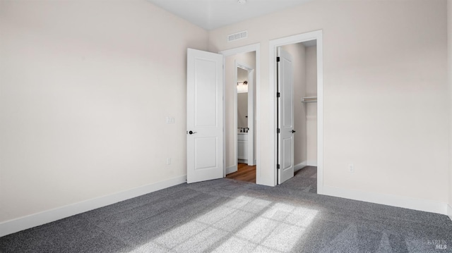 unfurnished bedroom with a spacious closet, dark colored carpet, and a closet