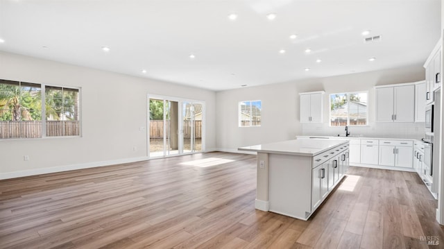 kitchen with light hardwood / wood-style floors, plenty of natural light, a kitchen island, and white cabinets