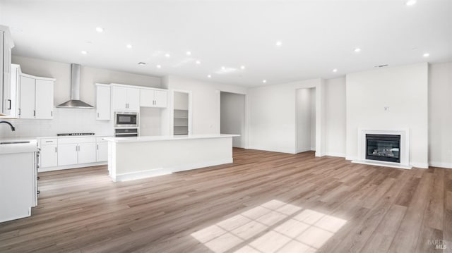 kitchen featuring wall chimney range hood, light hardwood / wood-style flooring, stainless steel appliances, a center island, and white cabinetry