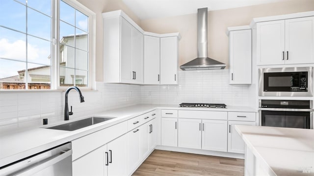 kitchen with white cabinets, appliances with stainless steel finishes, light hardwood / wood-style flooring, wall chimney exhaust hood, and sink