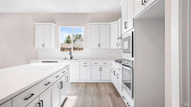 kitchen with appliances with stainless steel finishes, light hardwood / wood-style flooring, decorative backsplash, and white cabinets