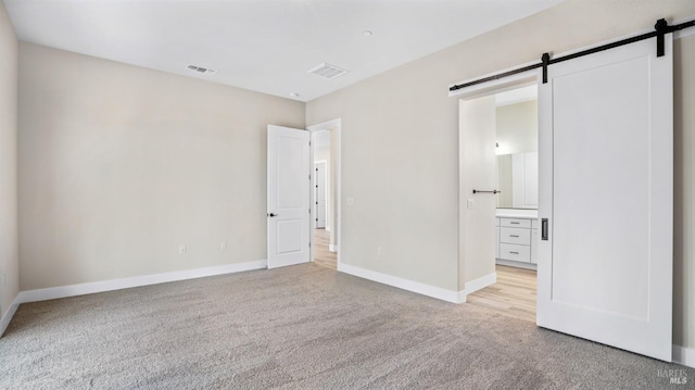 unfurnished bedroom featuring ensuite bathroom, light carpet, and a barn door