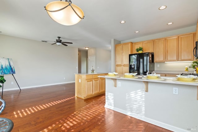 kitchen featuring light brown cabinets, dark hardwood / wood-style floors, a breakfast bar area, a center island, and black fridge with ice dispenser