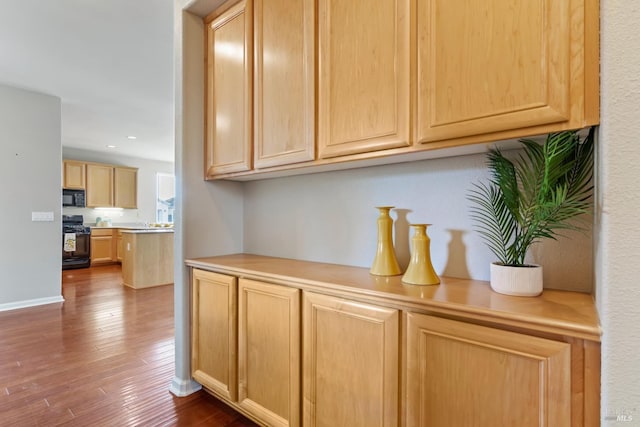 kitchen with black appliances, light brown cabinets, and dark hardwood / wood-style floors