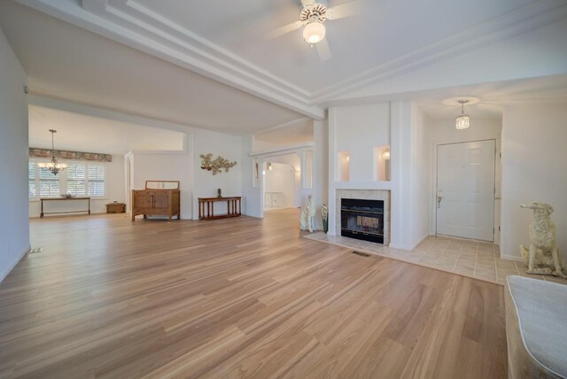 unfurnished living room with a tiled fireplace, vaulted ceiling, ceiling fan with notable chandelier, and light hardwood / wood-style floors