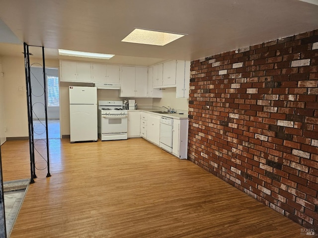 kitchen with brick wall, white appliances, under cabinet range hood, a sink, and light wood finished floors
