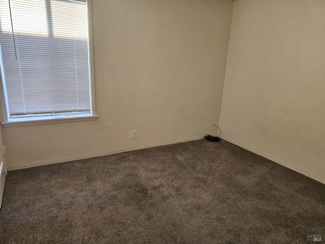 spare room featuring baseboards and dark colored carpet