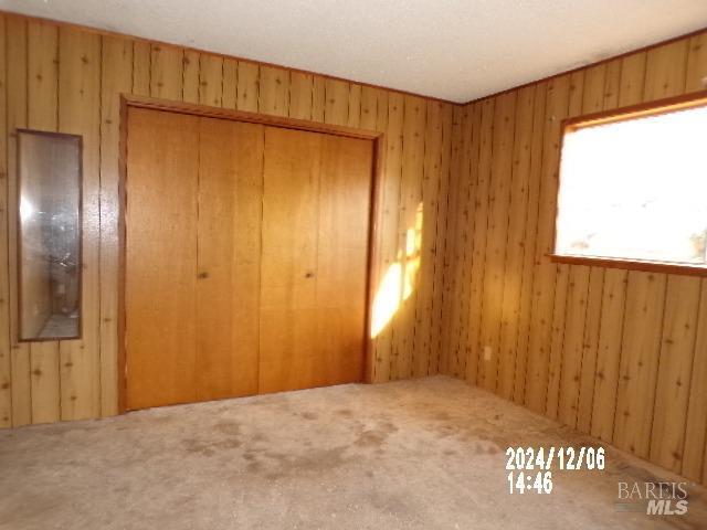 unfurnished bedroom featuring wooden walls, a closet, and carpet floors