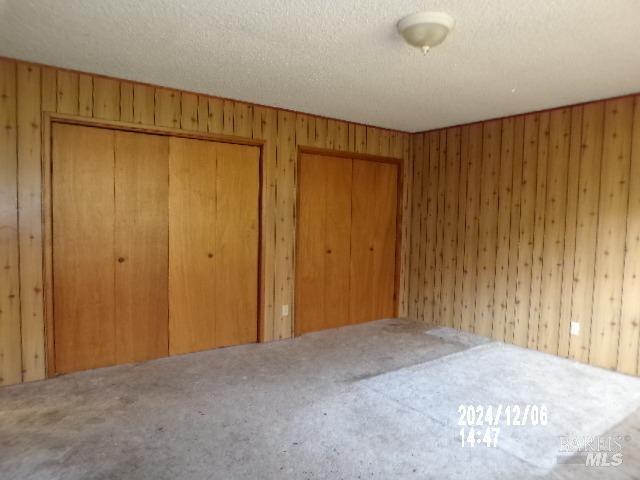 unfurnished bedroom with a textured ceiling, multiple closets, and wooden walls