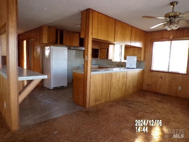 kitchen with kitchen peninsula, white fridge, ceiling fan, and wooden walls