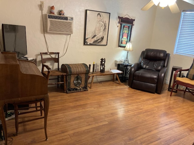 sitting room featuring a ceiling fan, wood finished floors, a textured wall, and a wall mounted AC